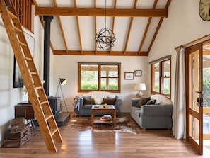 A spacious living room with wooden beams, a fireplace, a sofa, a coffee table, and a ladder.