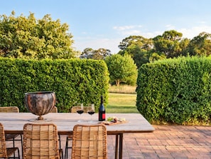 Un área de comedor al aire libre con una mesa, sillas, una botella de vino, copas y un tazón.