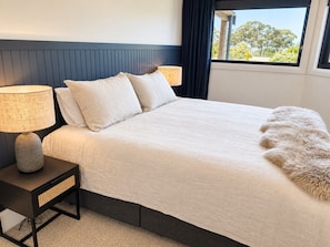 A bed with a white duvet, two pillows, a fluffy throw, and a nightstand with a lamp.
