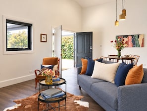 A living room with a sofa, a coffee table, and a chair. There is a door leading to an outdoor area.