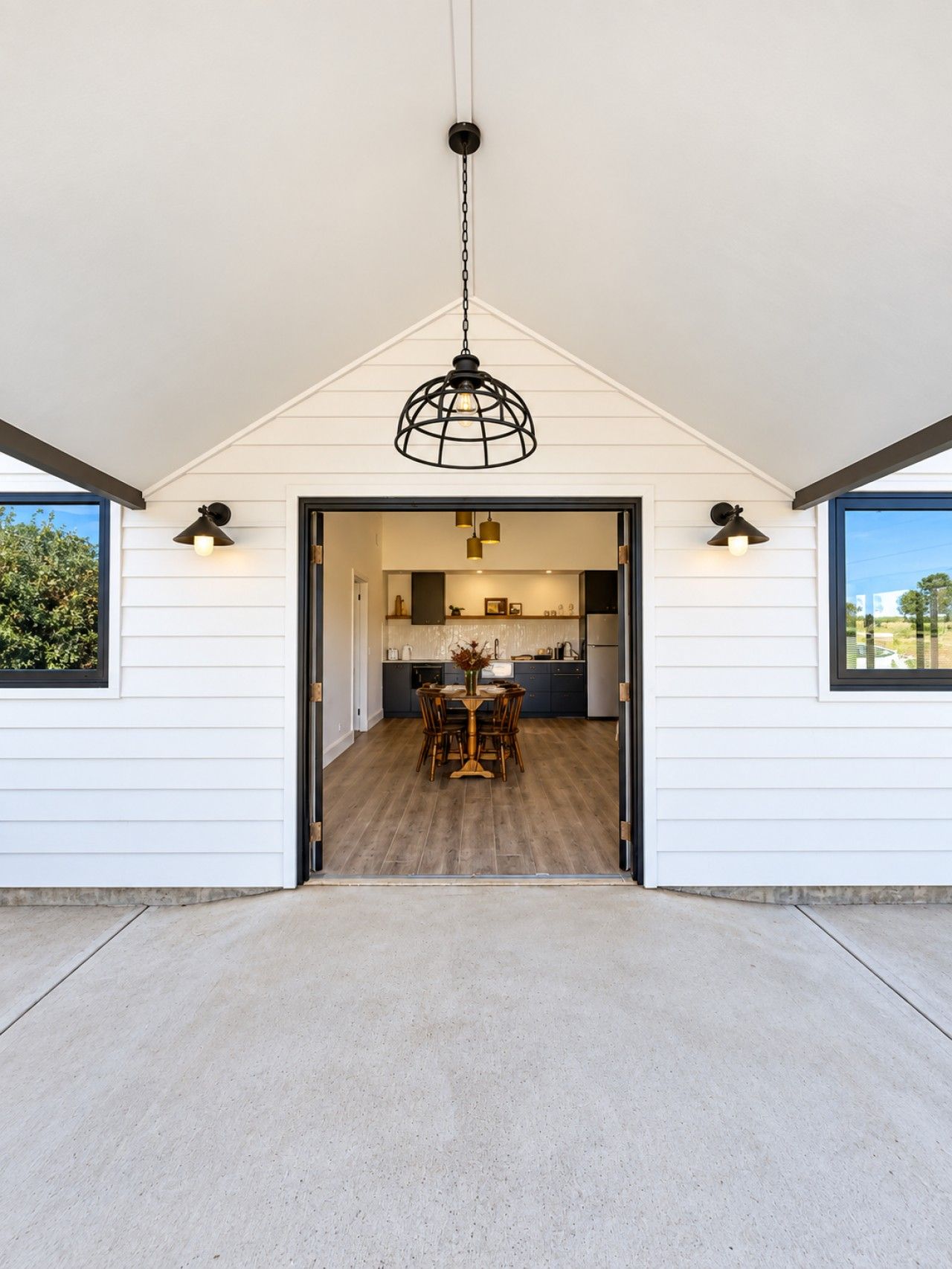 A modern kitchen with a dining area, white exterior walls, and a concrete floor.