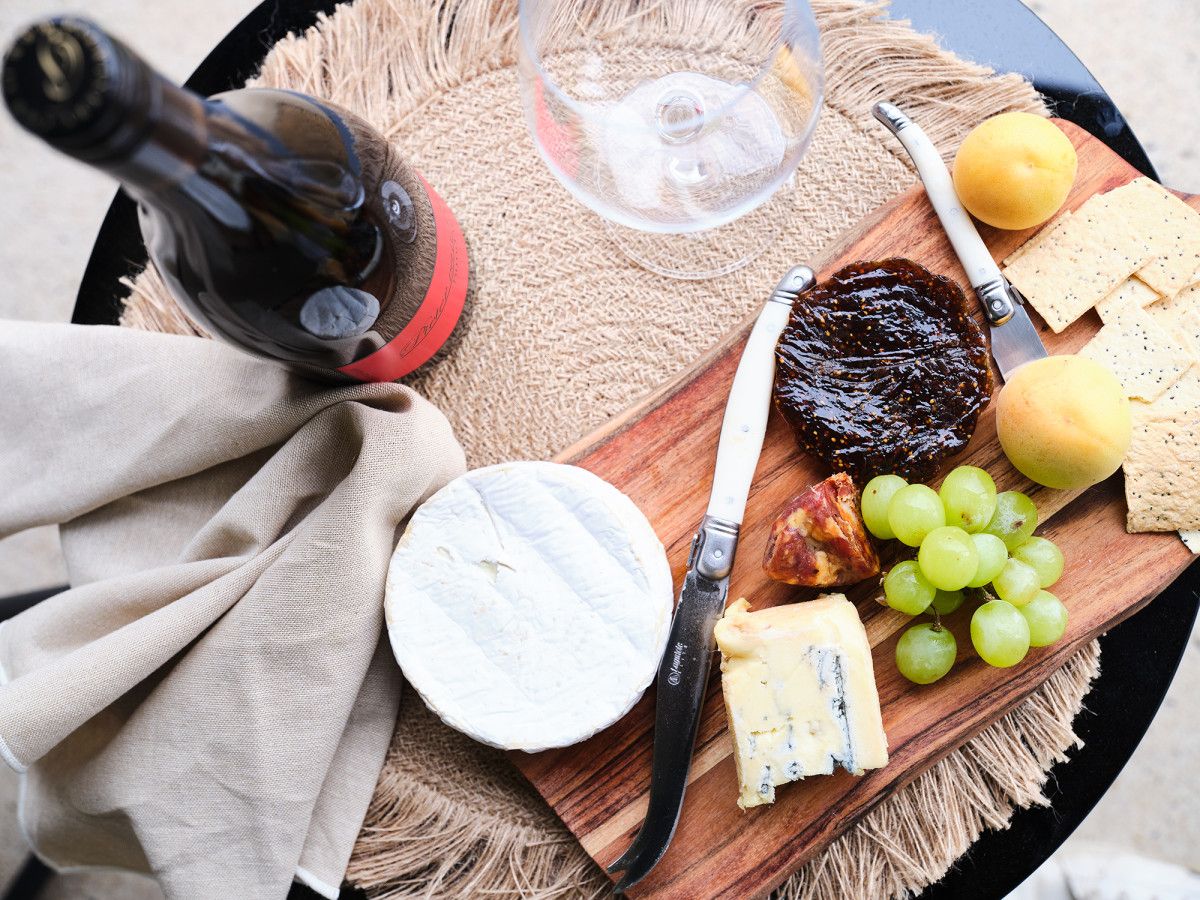 Una tabla de madera con varios quesos, uvas y una botella de vino sobre una mesa.