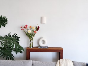 A room with a wooden console table, a vase with flowers, a book, and a wall-mounted light fixture.
