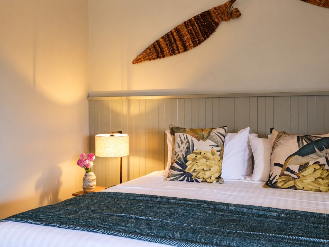 A hotel room with a bed, a nightstand with a lamp, and a wall-mounted decorative piece.