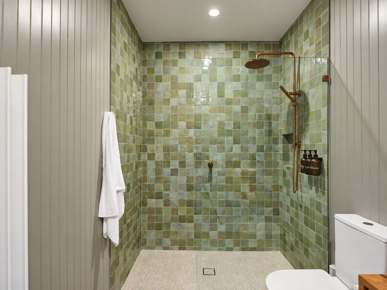 A bathroom with a shower, tiled walls, a towel hanging, and a toilet.