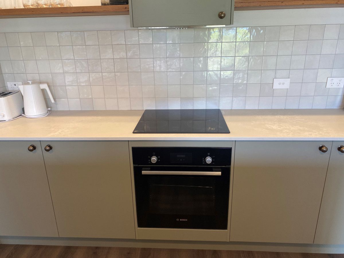 Una cocina con horno Bosch, salpicadero de azulejos blancos y armarios de colores claros.