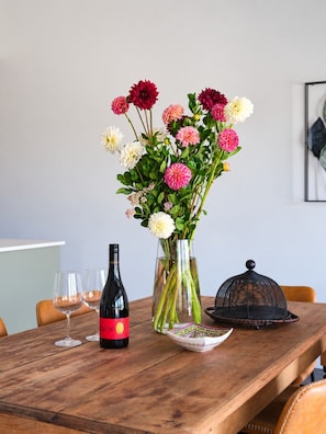 A wooden table with a wine bottle, two glasses, a vase with flowers, and a decorative bowl.