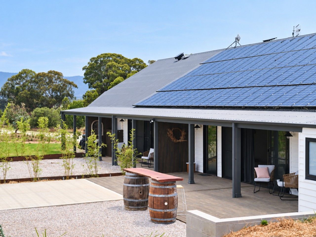 A modern house with a solar panel roof, a covered outdoor seating area, and a garden.