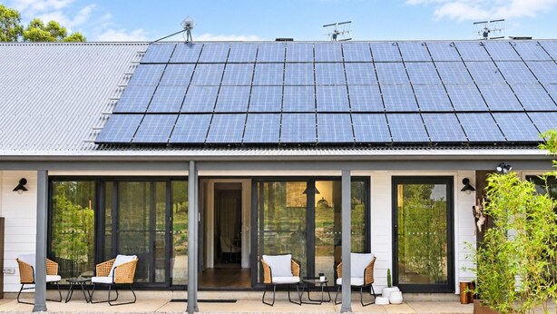 Ein Gebäude mit einer Photovoltaikanlage auf dem Dach, einer überdachten Terrasse mit Sitzgelegenheiten und einem Glastür-Eingang.