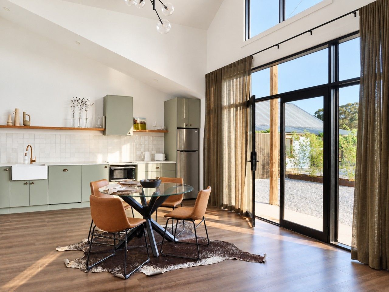 A modern kitchen with a dining area, large windows, and a view of the outdoors.
