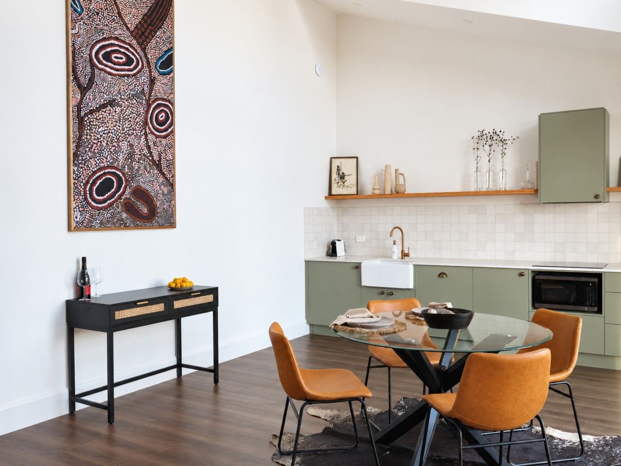A modern kitchen with a dining area, featuring a glass table and orange chairs.