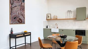 A modern kitchen with a dining area, featuring a glass table and orange chairs.