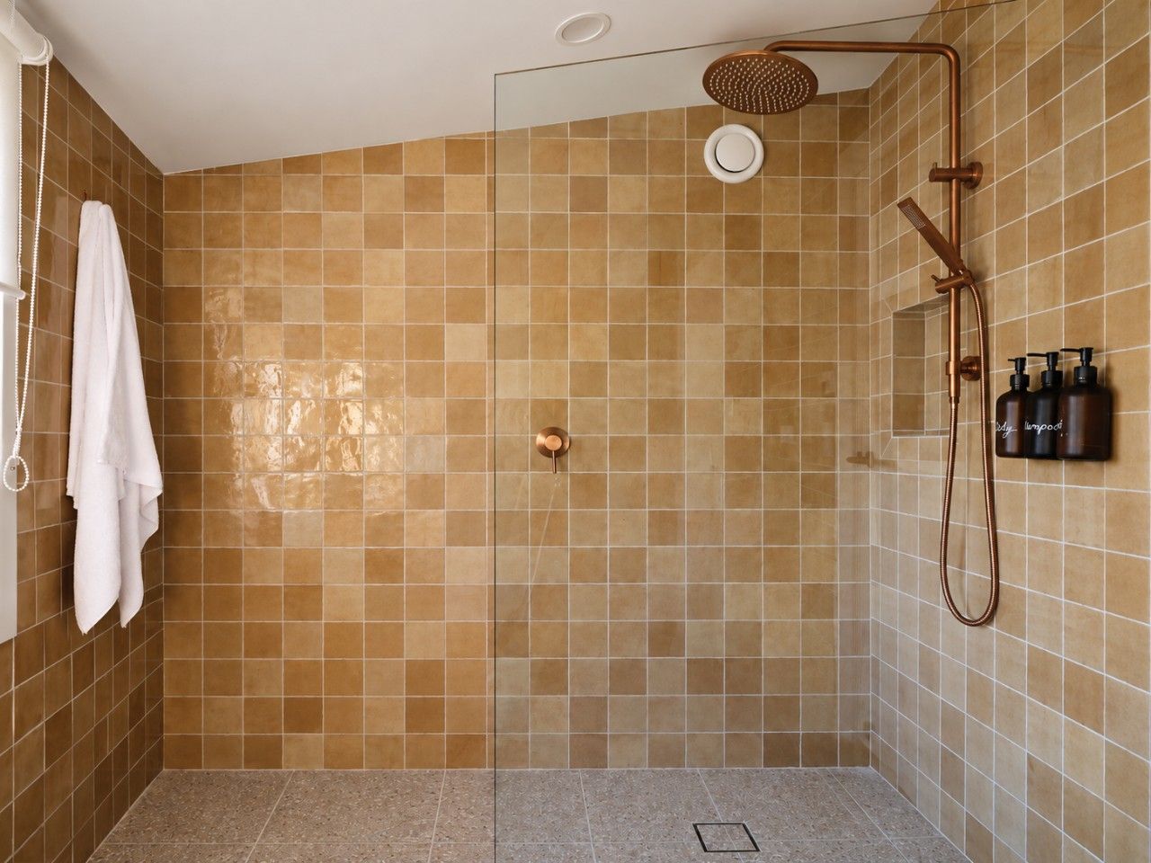 Ein Duschbereich mit Glastür, Handtuchhalter und einer am Wand befestigten Shampoo-Flasche.