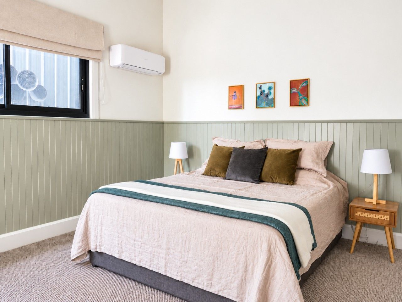 A bedroom with a bed, bedside lamps, a window with blinds, and wall-mounted artwork.