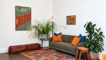Een woonkamer met een bank, een salontafel, een vloerkleed en twee planten.