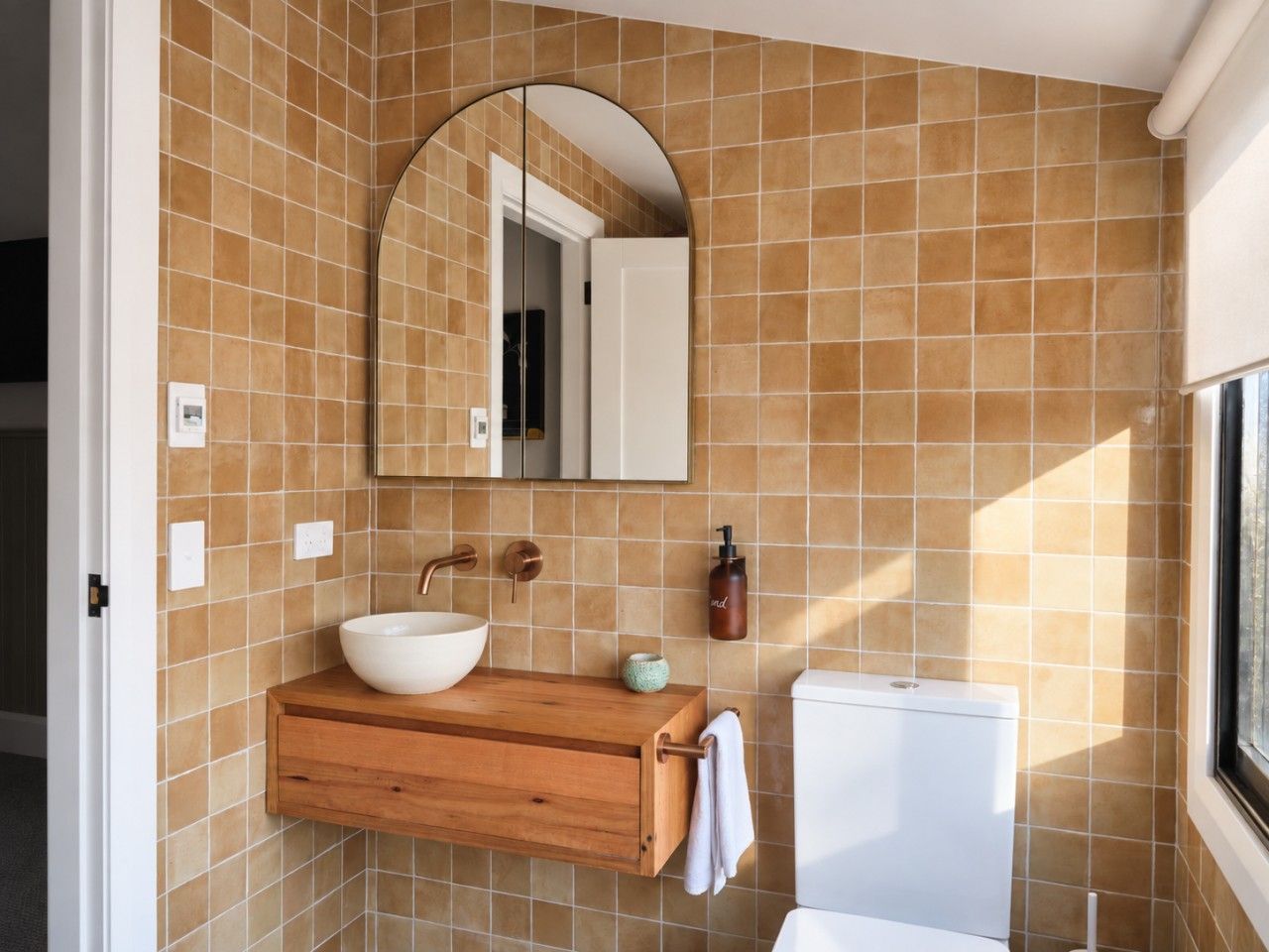 Un baño con un espejo grande, un mueble de tocador de madera, un lavamanos blanco y un inodoro.
