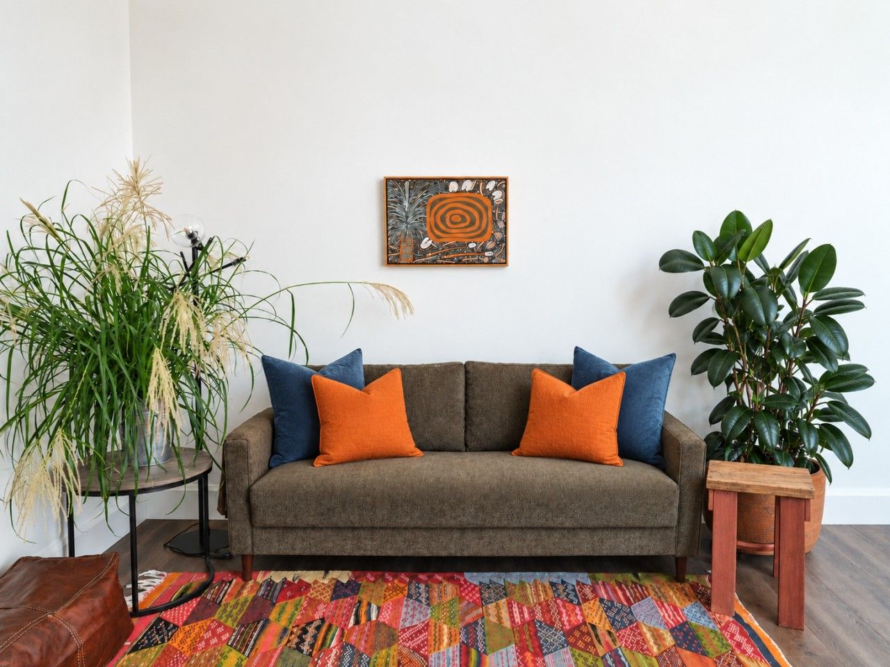 A living room with a sofa, pillows, a colorful rug, a plant, and a wall art piece.