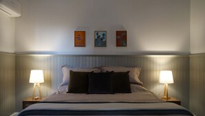 A neatly made bed with a headboard, two bedside lamps, and three framed artworks on the wall.