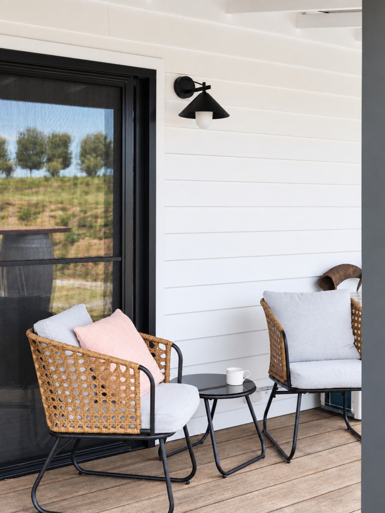 A balcony with wicker chairs, a small table, and a wall-mounted light fixture.