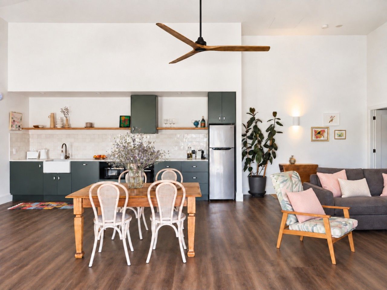A modern kitchen with dark cabinets, a wooden dining table, and white chairs.