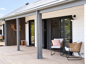 Un espace extérieur abrité doté d’une terrasse en bois, de deux fauteuils en osier et d’une porte vitrée donnant sur une pièce.