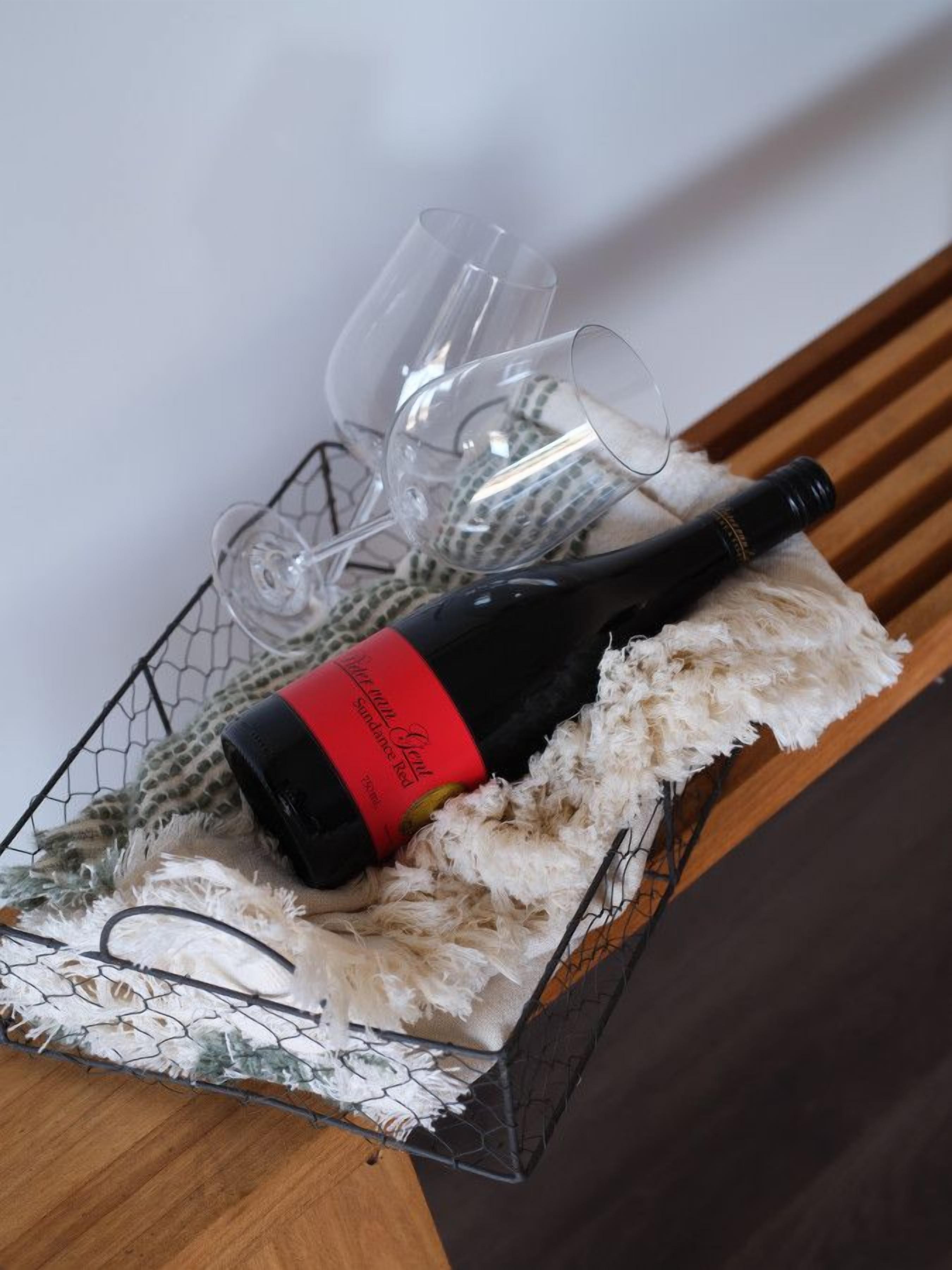 A wine bottle with a red label on a wire basket filled with white feathers and two empty wine glasses.