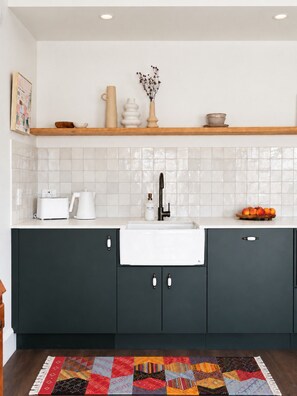 Une cuisine moderne avec des meubles de couleur sombre, un évier blanc et un dosseret carrelé.