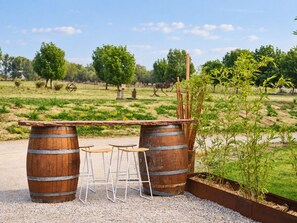 Un espacio de descanso al aire libre rústico con dos barriles de madera, una mesa de madera y tres taburetes.