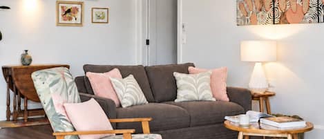 Een moderne woonkamer met een grijze bank, een fauteuil met patroon, een kleine ronde tafel met een lamp en een kuitenvachttapijt.