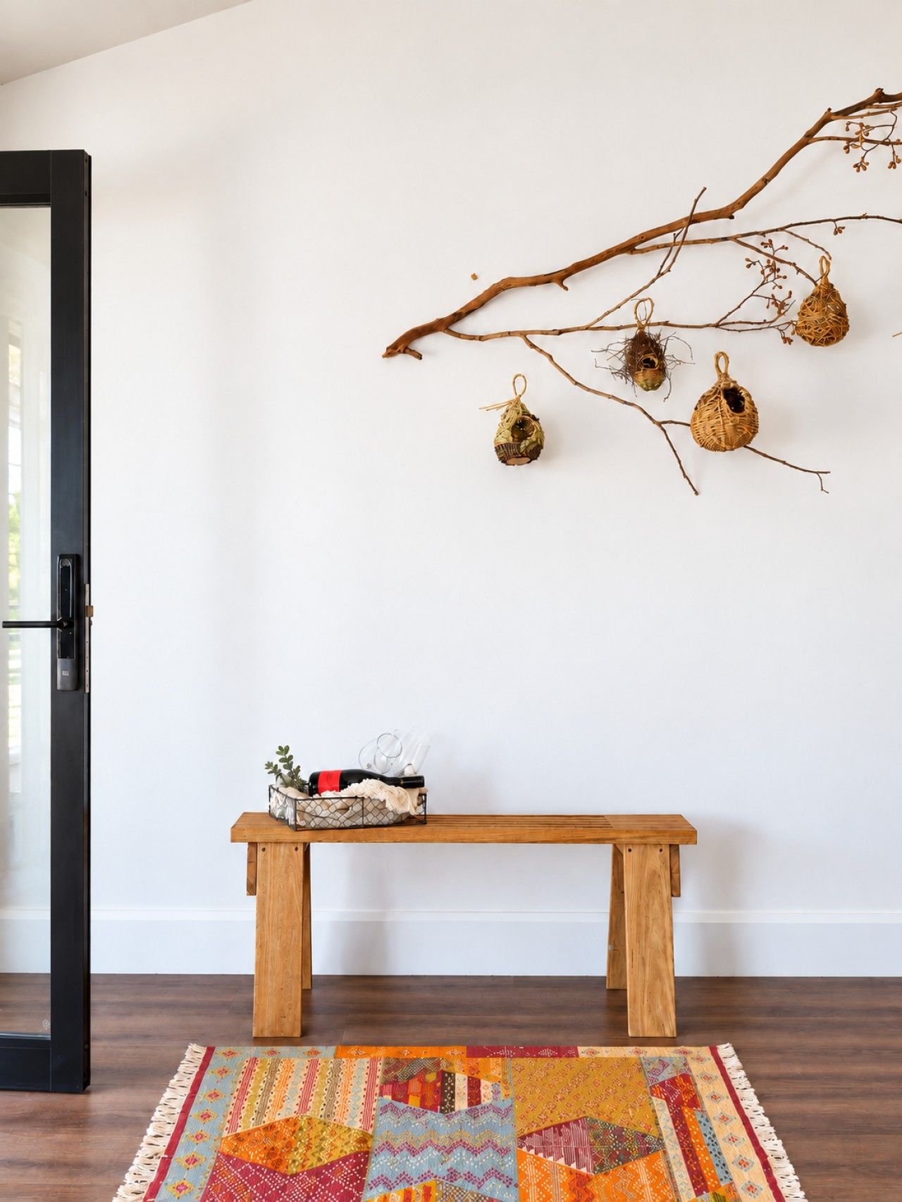 A room with a wooden bench, a colorful rug, and a branch with decorative birdcages.