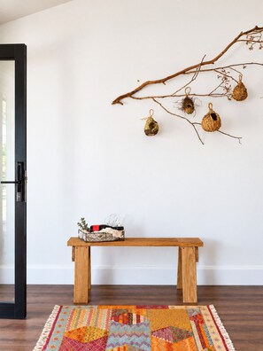 Une pièce avec un banc en bois, un tapis coloré et une branche ornée de cages à oiseaux décoratives.