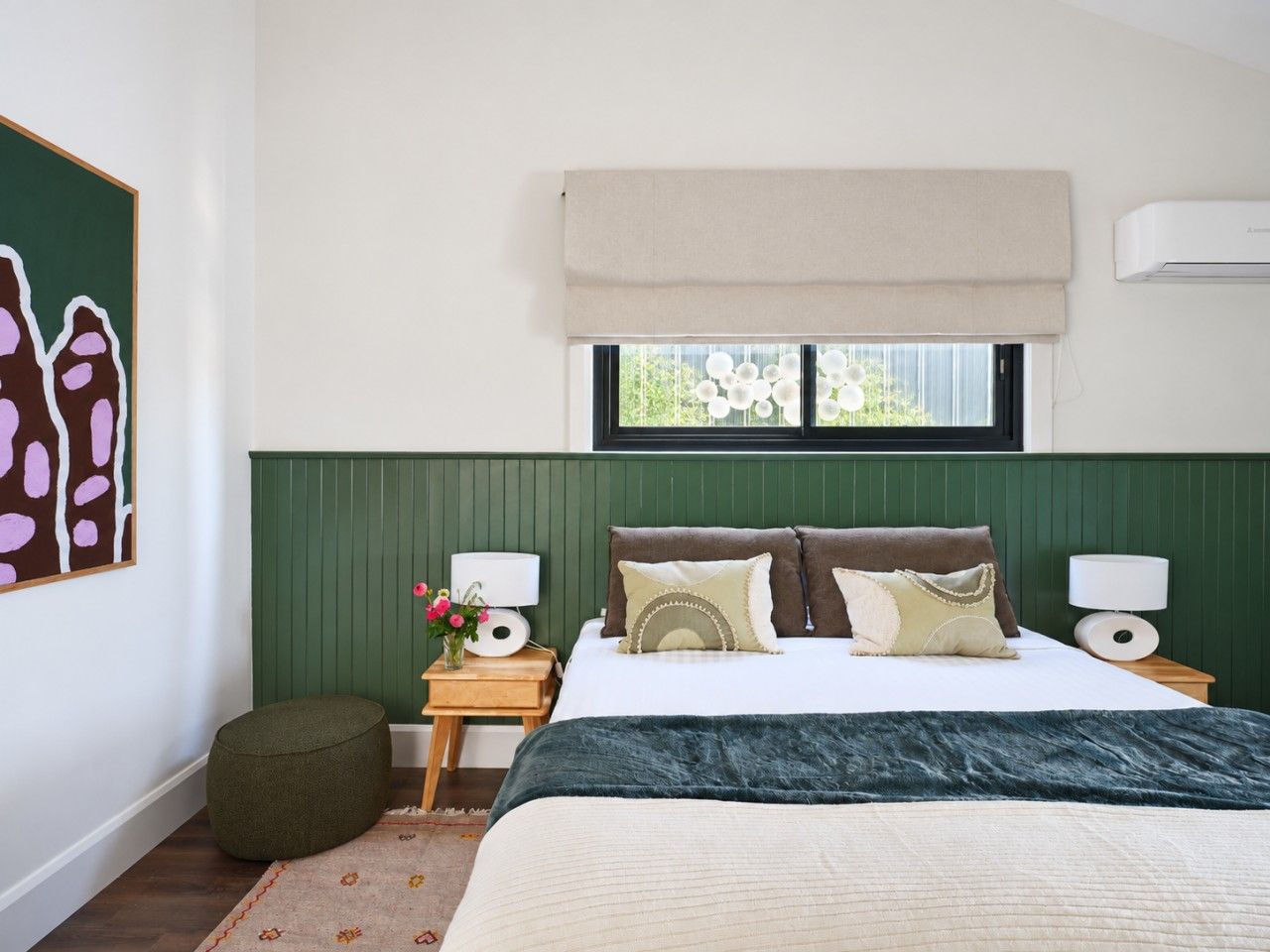A bedroom with a bed, bedside tables, a window with a view, and a green headboard.