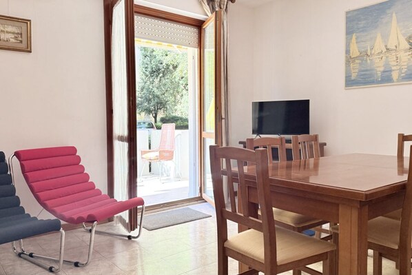 A room with a wooden dining table, chairs, a television, and a red chair.