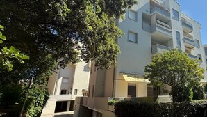 Un edificio residencial de varios pisos con balcones, un acceso cubierto y vegetación circundante.