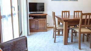 Un comedor con una mesa y sillas de madera, un televisor sobre un mueble bajo y un cuadro en la pared.