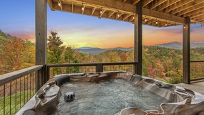 Un bain à remous avec une terrasse en bois et une vue sur le feuillage automnal et les montagnes.