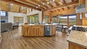 Une cuisine spacieuse, dotée de meubles en bois, d’un îlot central et de grandes fenêtres offrant une vue sur l’extérieur.