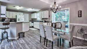 A modern kitchen with white cabinets, a glass dining table, and a chandelier. - 30A Private Pool Cottage with Pool and Golf Cart! (Santa Rosa Beach)