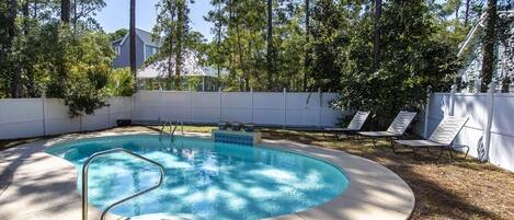 A circular swimming pool with a metal ladder, surrounded by a white fence, and shaded by trees.
