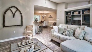 A living room with a sofa, coffee table, and a ceiling fan. There is a dining area in the background with chairs and a table. - 30A Private Pool Cottage with Pool and Golf Cart! (Santa Rosa Beach)