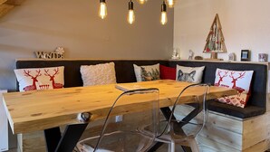 Un coin repas chaleureux avec une table en bois, des chaises transparentes et un banc agrémenté de coussins à motifs de rennes.