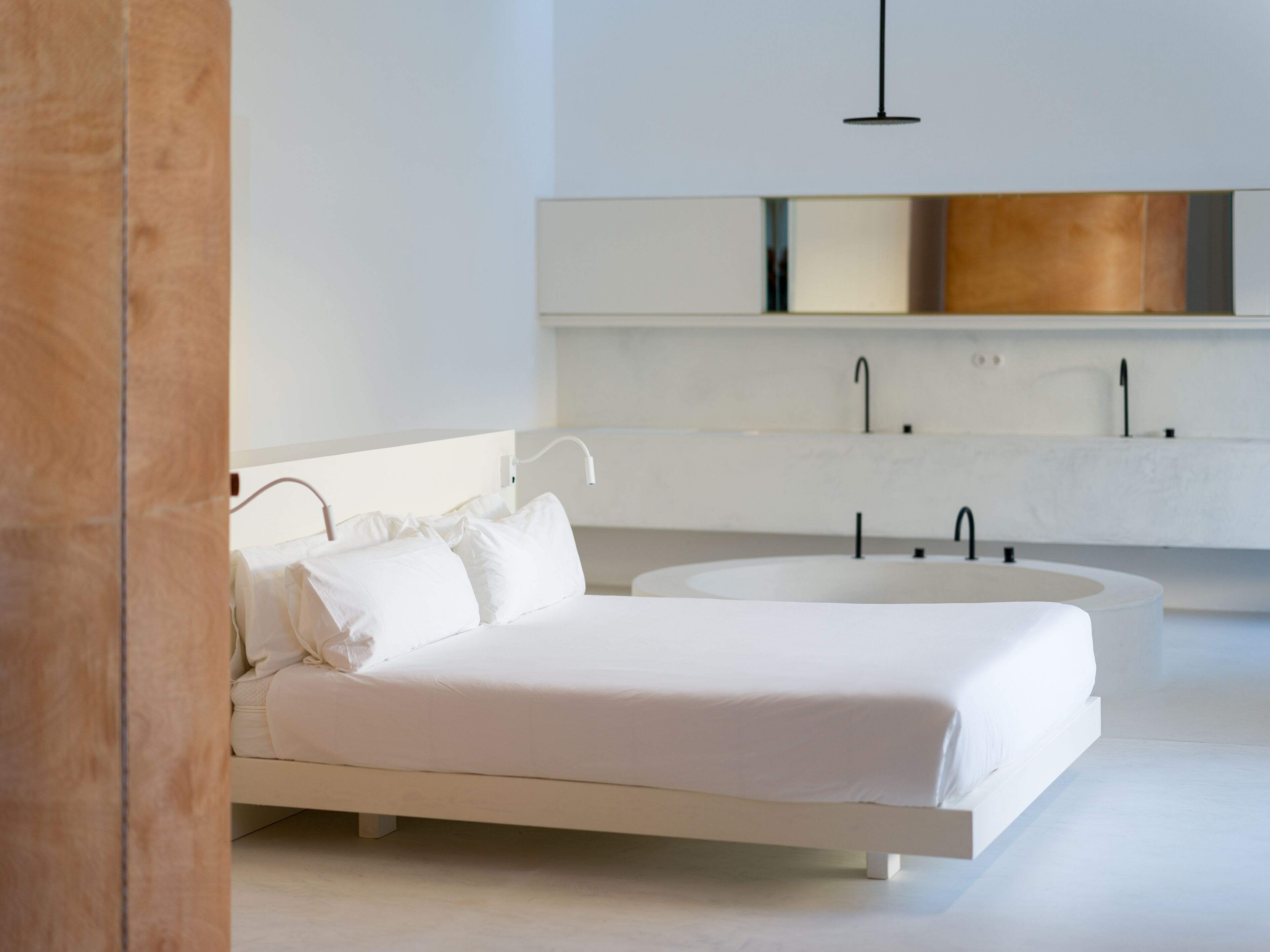 A modern bedroom with a bed, a large round bathtub, and a white vanity with a mirror.