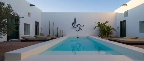 A modern outdoor pool area with a minimalist design, featuring a central pool, lounge seating, and a decorative wall with abstract art.