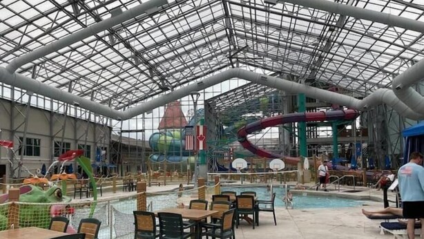 Un parque acuático interior con techo de vidrio, toboganes, piscina y zonas de descanso.