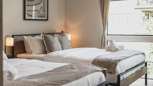 Hotellihuone, jossa on kaksi sänkyä, seinällä kehystetty abstrakti taideteos ja suuri ikkuna, jossa on verhot.