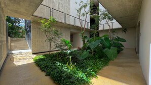 A modern building with a concrete exterior, a staircase leading to an upper level, and a small garden area with various plants. - Luxury Studio-private individual pool (Tulum)