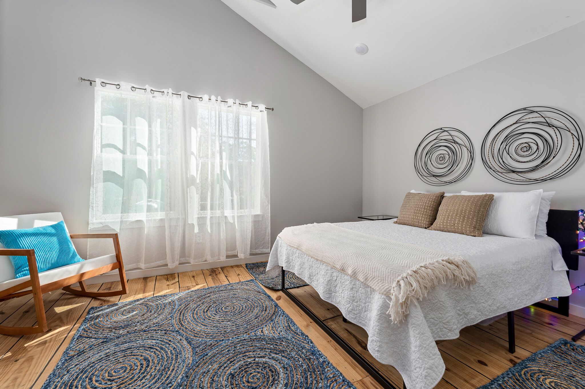 Une chambre à coucher avec un grand lit, un fauteuil à bascule, un tapis bleu et deux œuvres d’art murales.