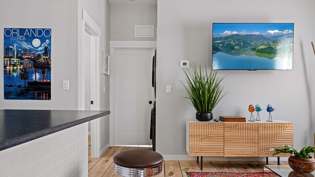 Eine moderne Küche mit schwarzem Arbeitsplatz, zwei Barhocker, einem Holzschrank und einem Fernseher, der eine Berglandschaft zeigt.