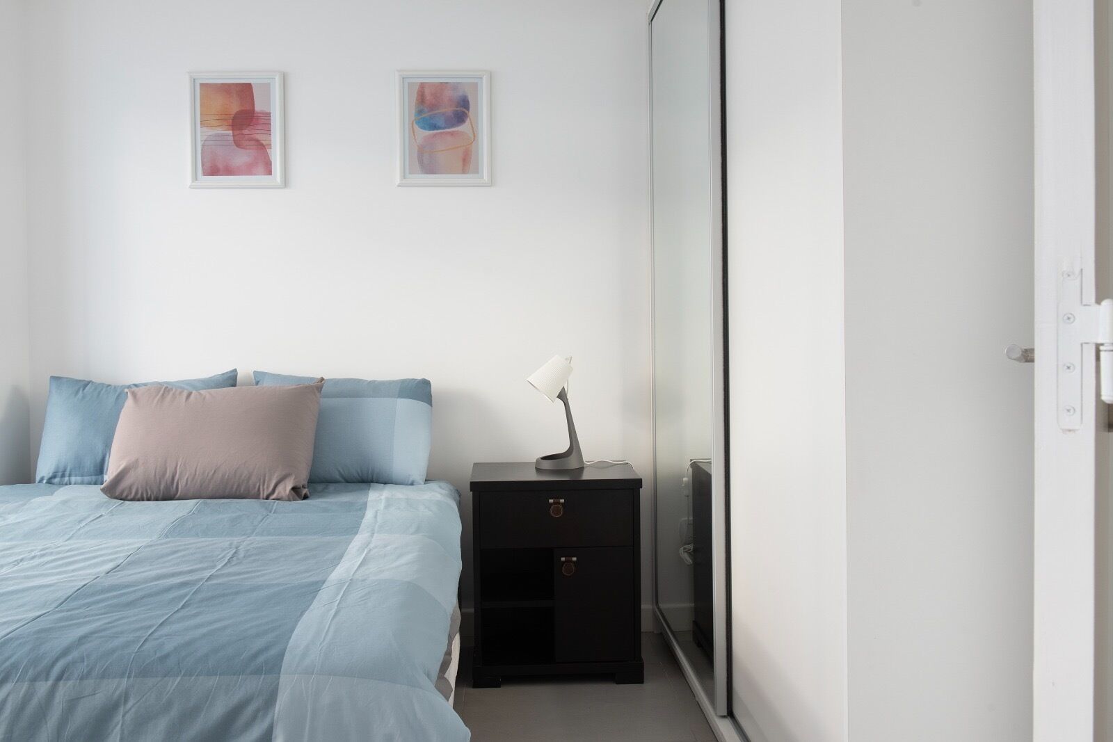 Ein Schlafzimmer mit einem Bett, Kissen, einem Nachttisch und zwei gerahmten Kunstwerken an der Wand.
