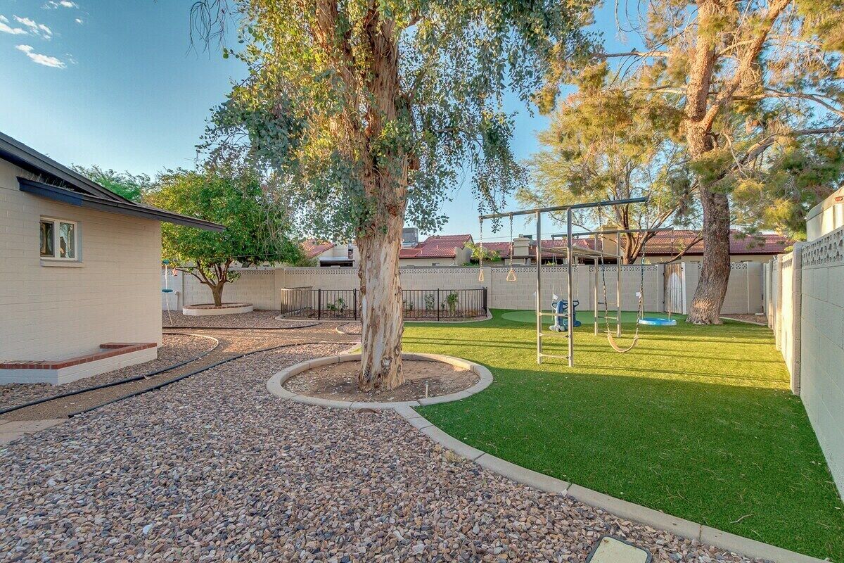 A backyard with a swing set, a tree, and a well-maintained lawn.